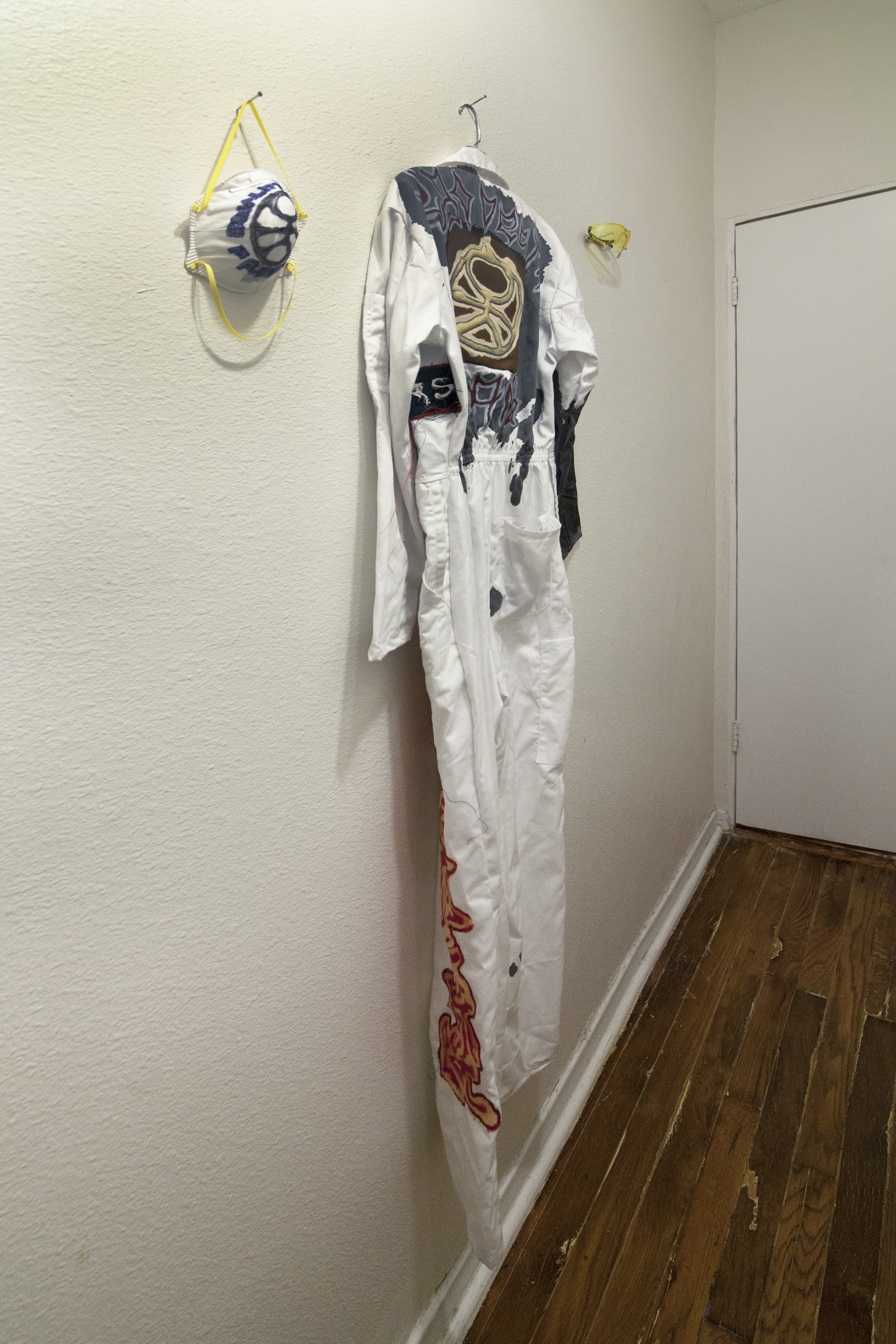 A white jumpsuit and resperator with drawings on them hung on a white wall